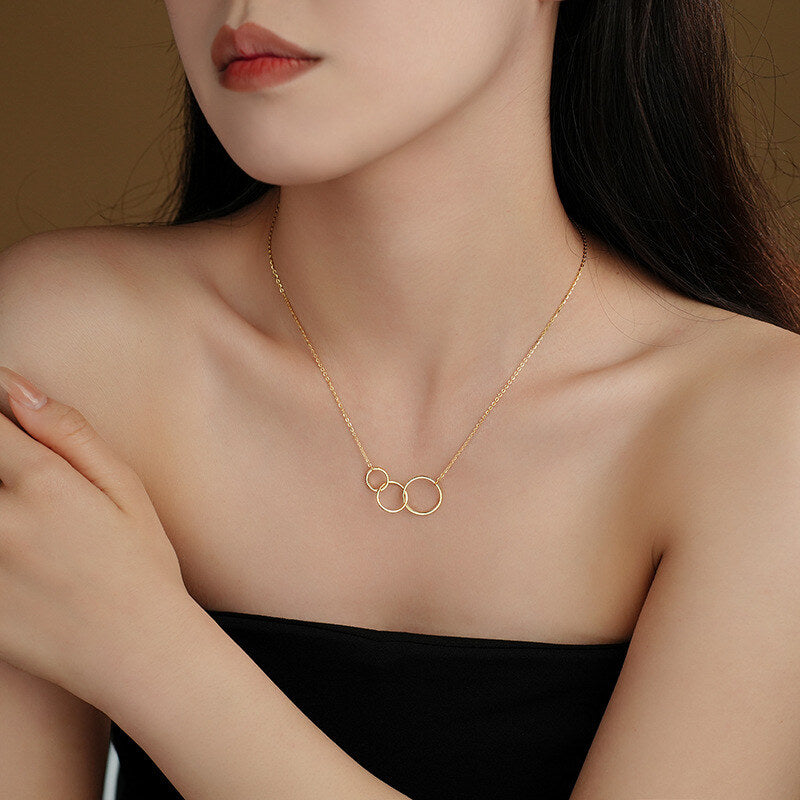 Woman wearing a gold necklace with three interlocking rings against a neutral background