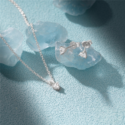 Silver necklace and earrings on a textured blue surface with clear crystals.