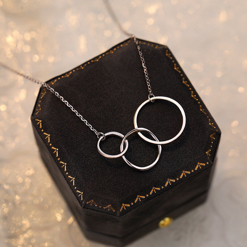 Silver necklace with interlocking rings on a decorative black stand with gold accents.