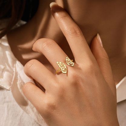 Gold ring with leaf design on a person's finger against a neutral background