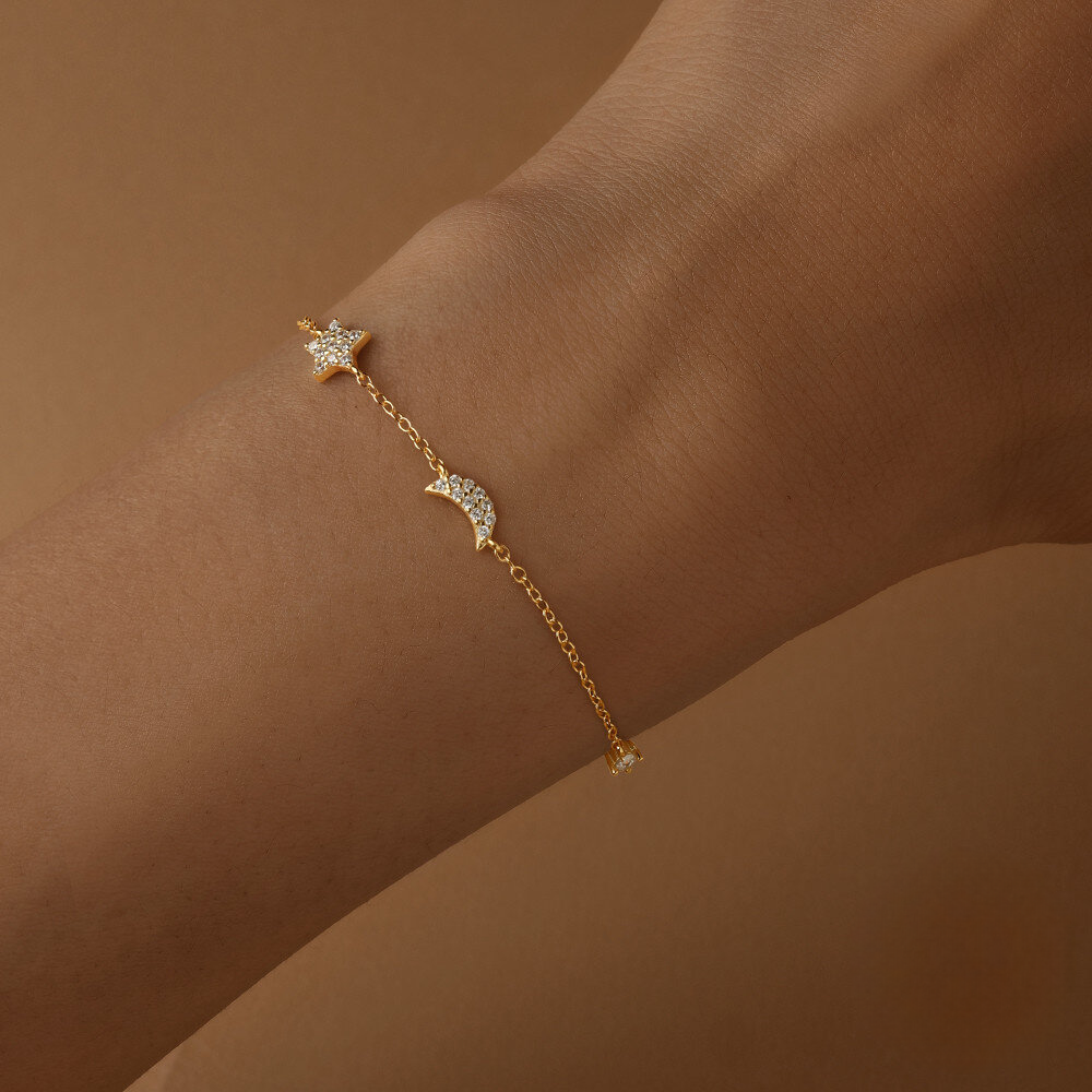 Gold bracelet with star and moon charms on a wrist against a brown background