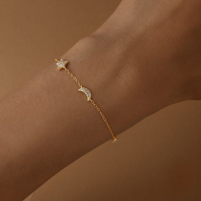 Gold bracelet with star and moon charms on a wrist against a brown background