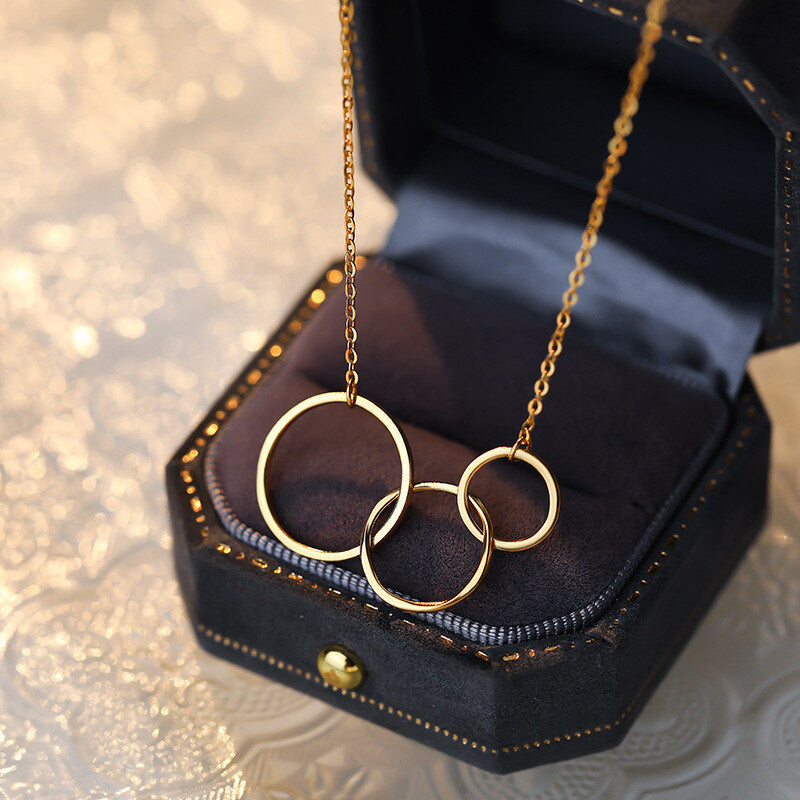Gold necklace with interlocking rings in a jewelry box on a textured surface