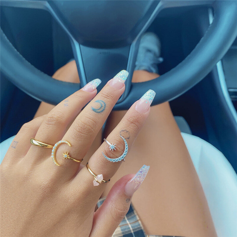 Hand with multiple rings and decorative nails in front of a steering wheel
