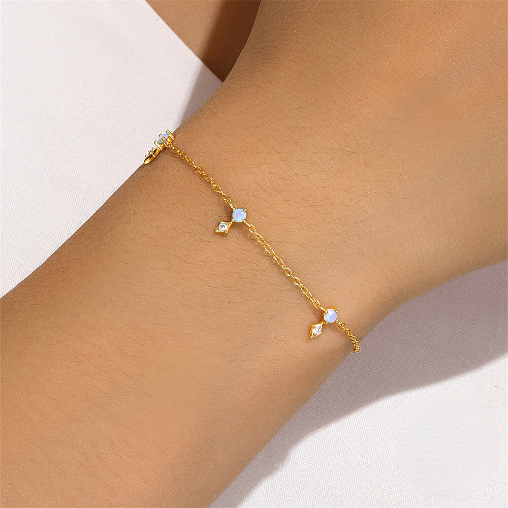 Gold anklet with small gemstones on a person's ankle against a neutral background