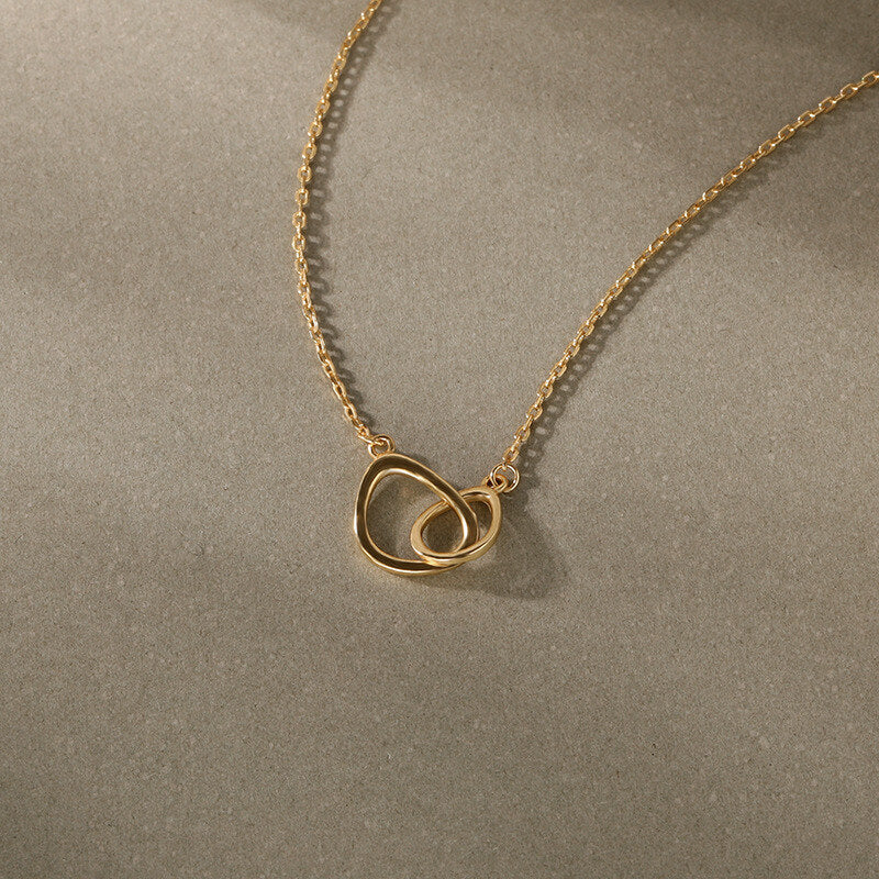 Gold necklace with a heart-shaped pendant on a beige background