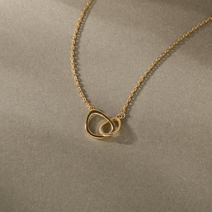 Gold necklace with a heart-shaped pendant on a beige background