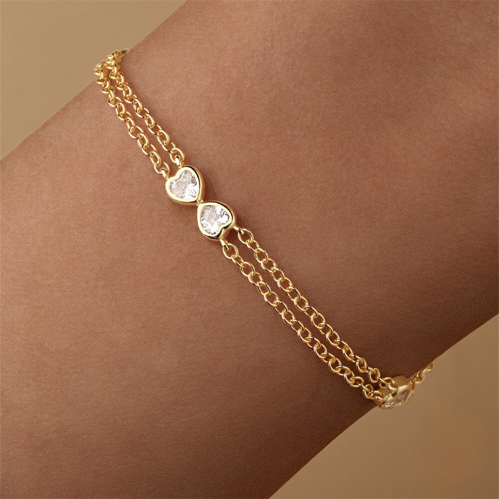 Gold bracelet with heart-shaped charms on a wrist against a beige background