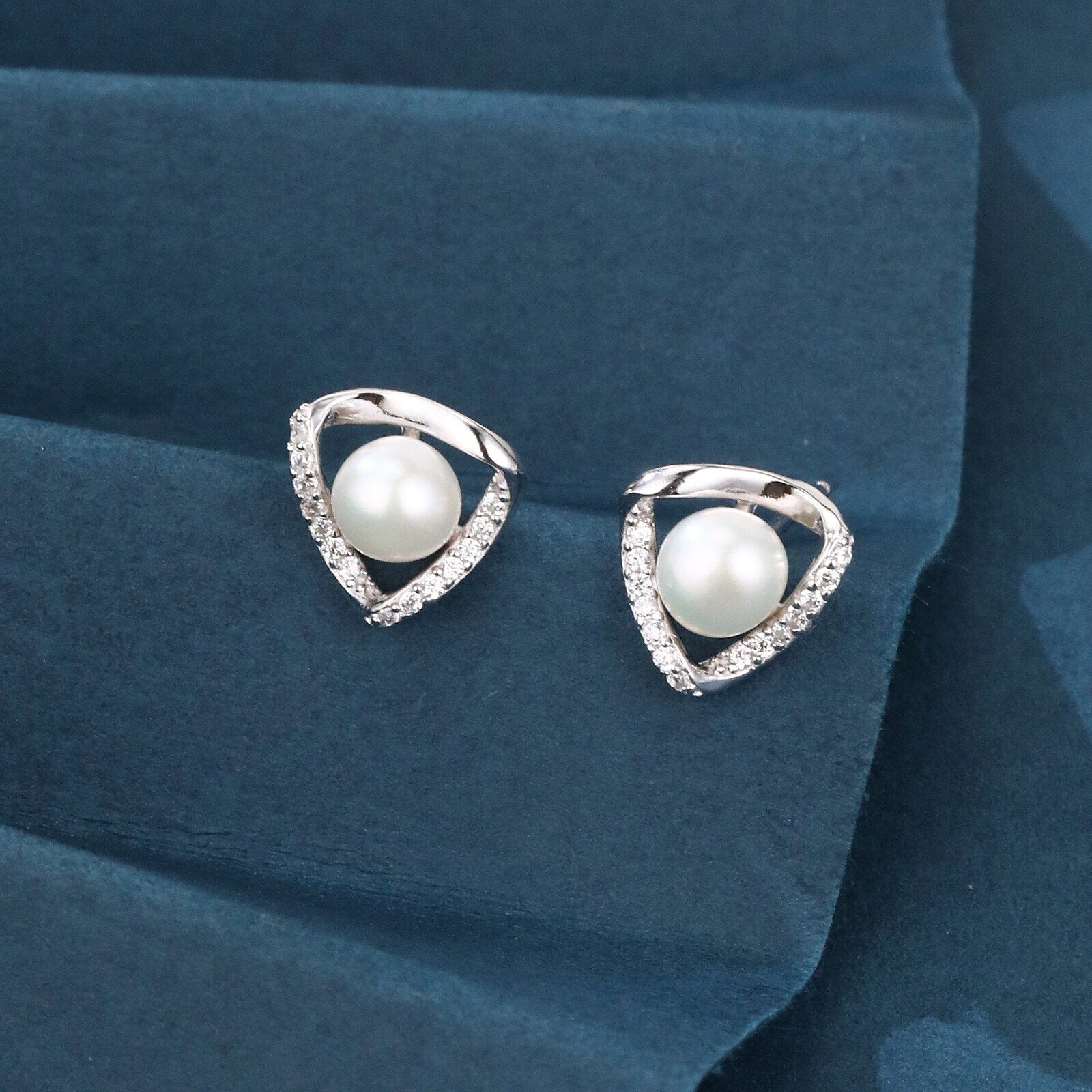 Pearl earrings with silver teardrop-shaped frames on a blue fabric background