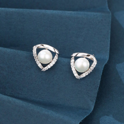 Pearl earrings with silver teardrop-shaped frames on a blue fabric background