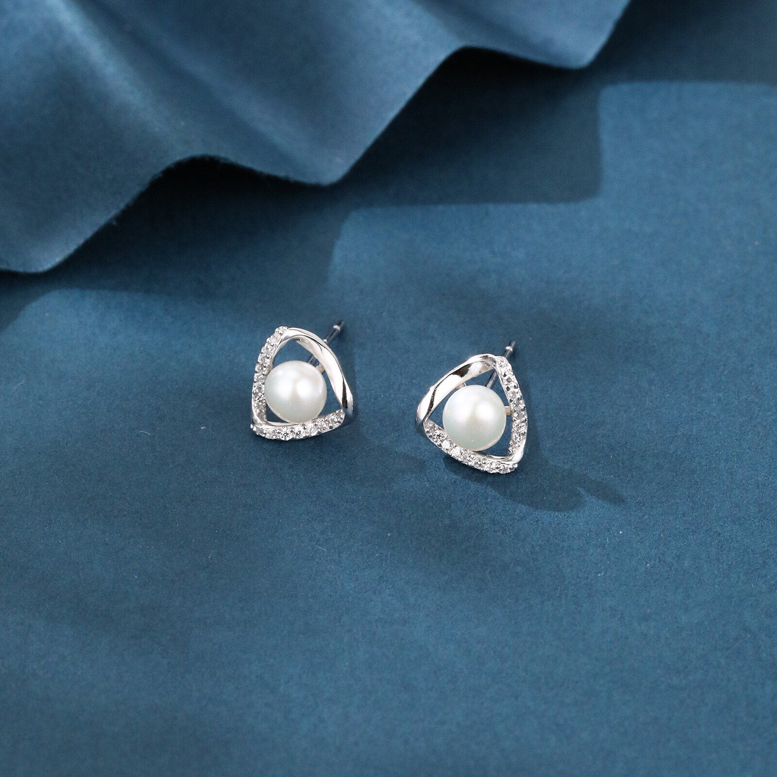 Pearl earrings with silver triangular setting on a blue fabric background