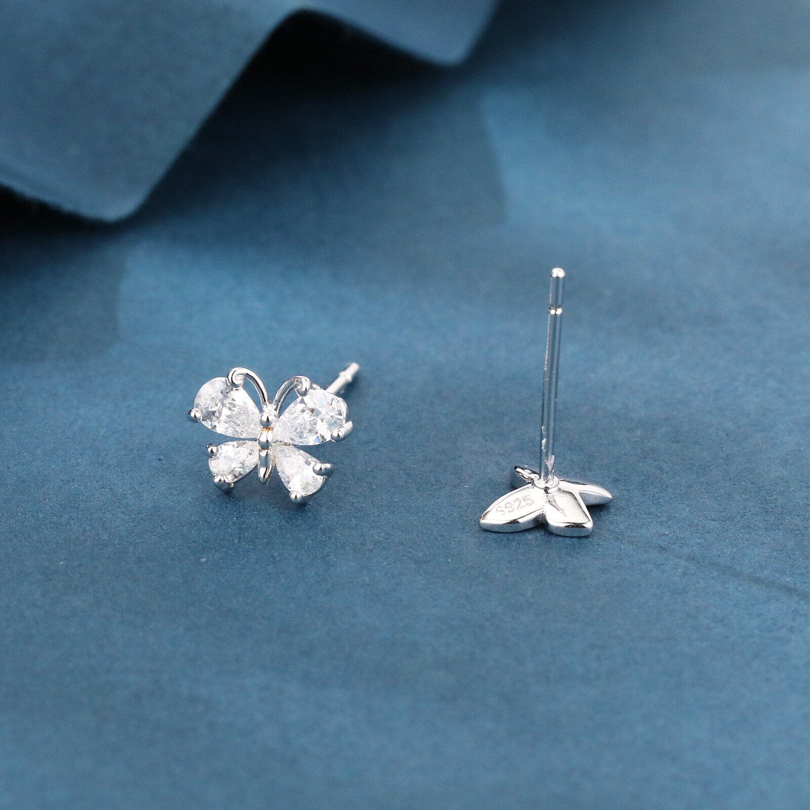 Butterfly-shaped silver earrings on a blue fabric background
