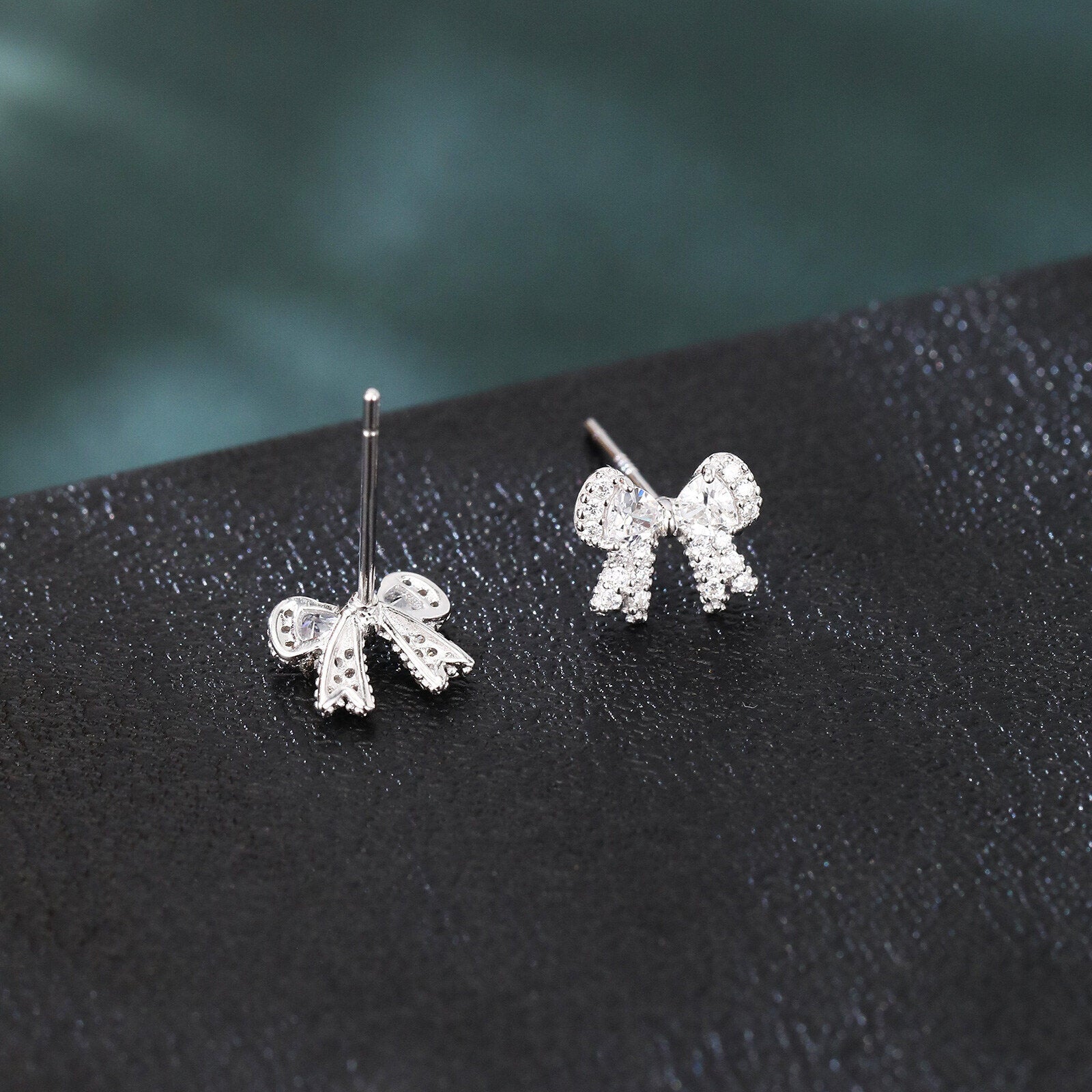 Silver bow-shaped earrings on a dark surface with a blurred green background