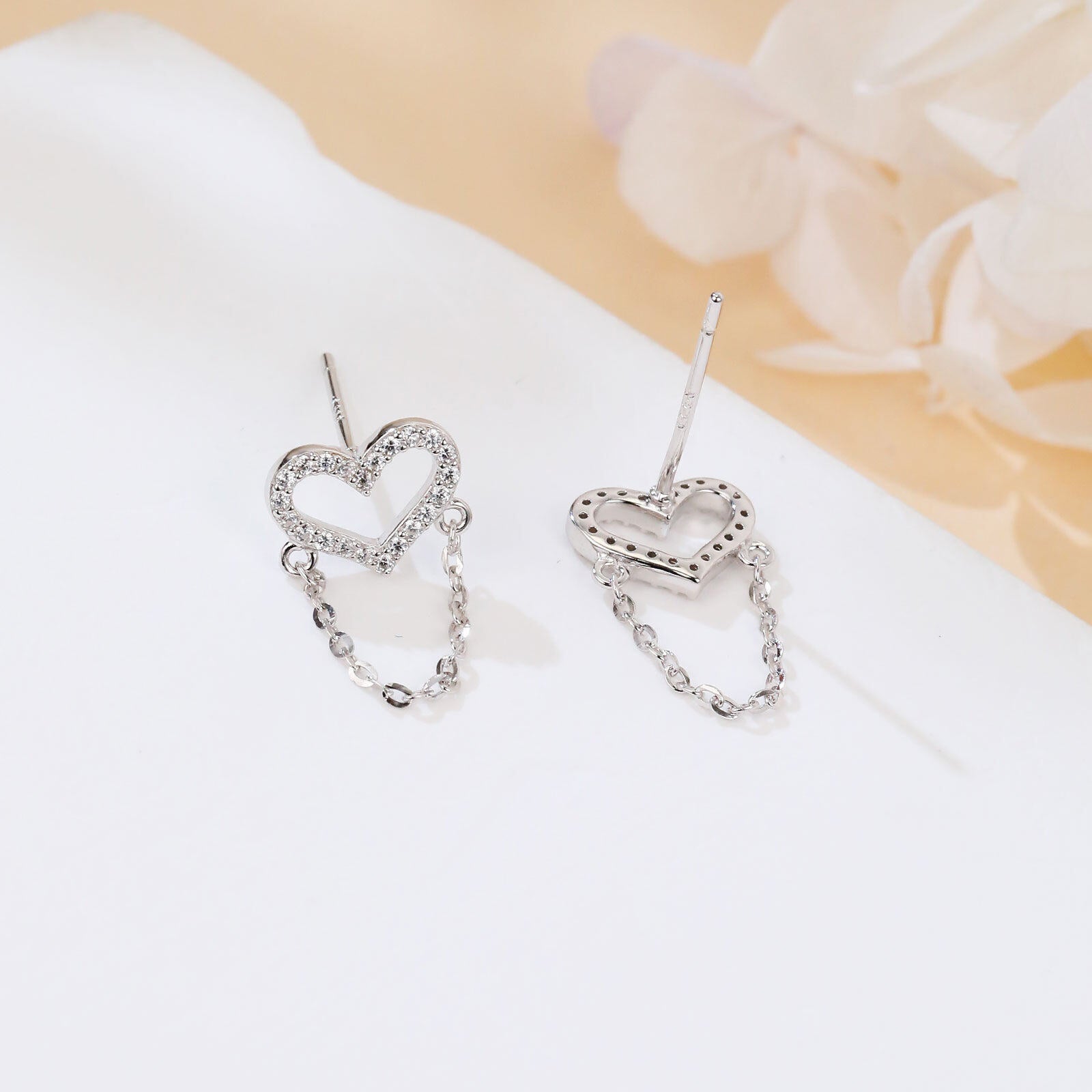 Heart-shaped earrings with chain details on a white surface with a floral background