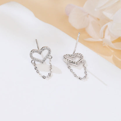 Heart-shaped earrings with chain details on a white surface with a floral background