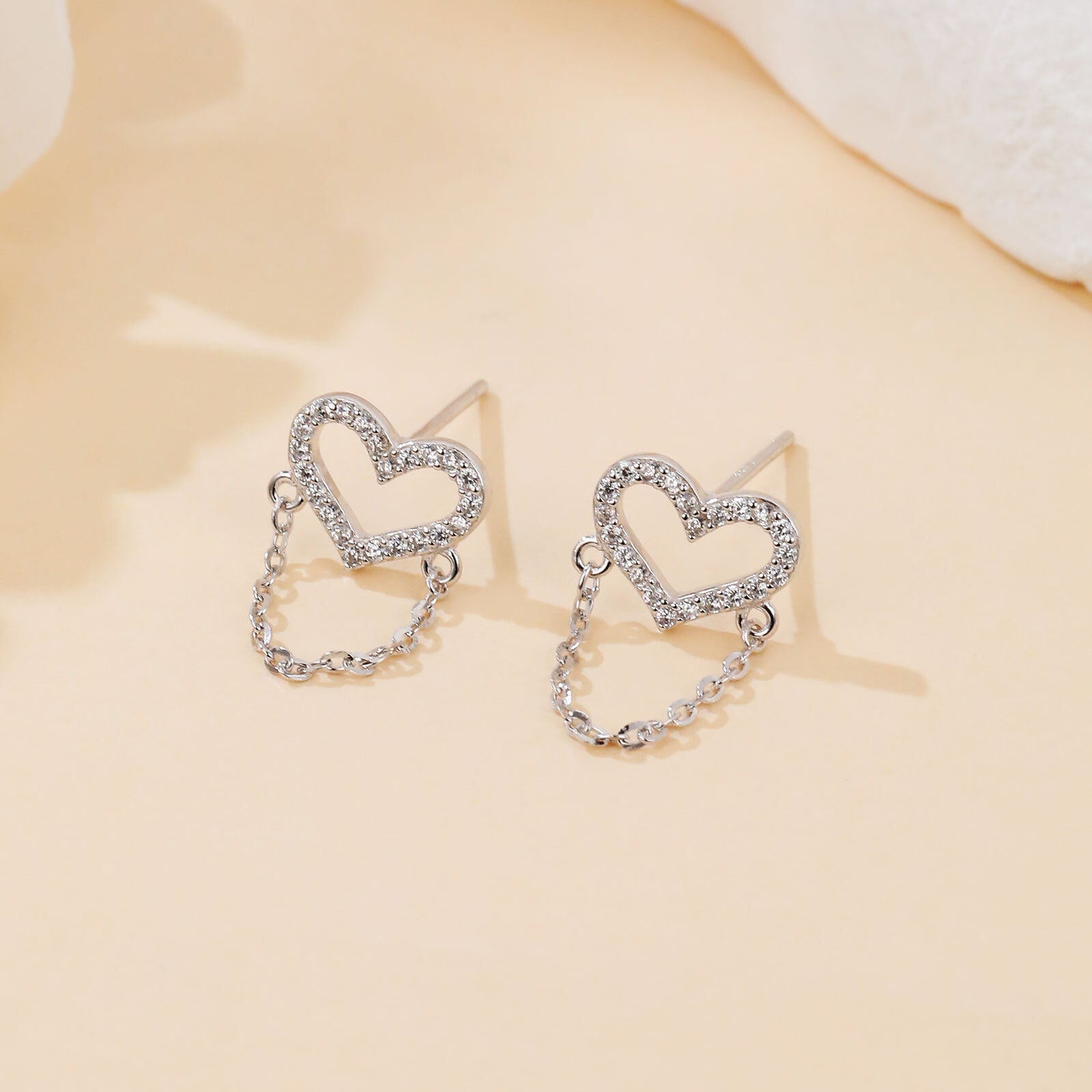 Heart-shaped earrings with chain details on a beige background