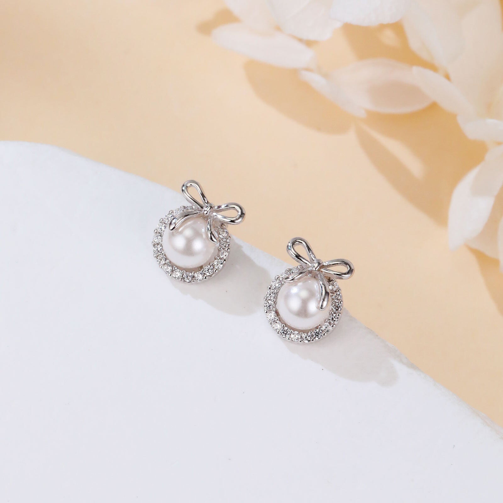 Pearl earrings with silver accents on a white surface with a beige background