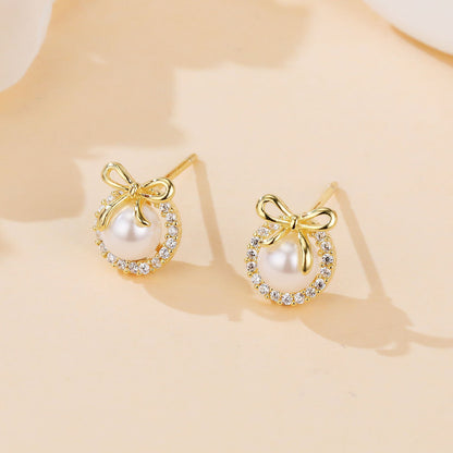 Gold earrings with pearl and bow design on a beige background