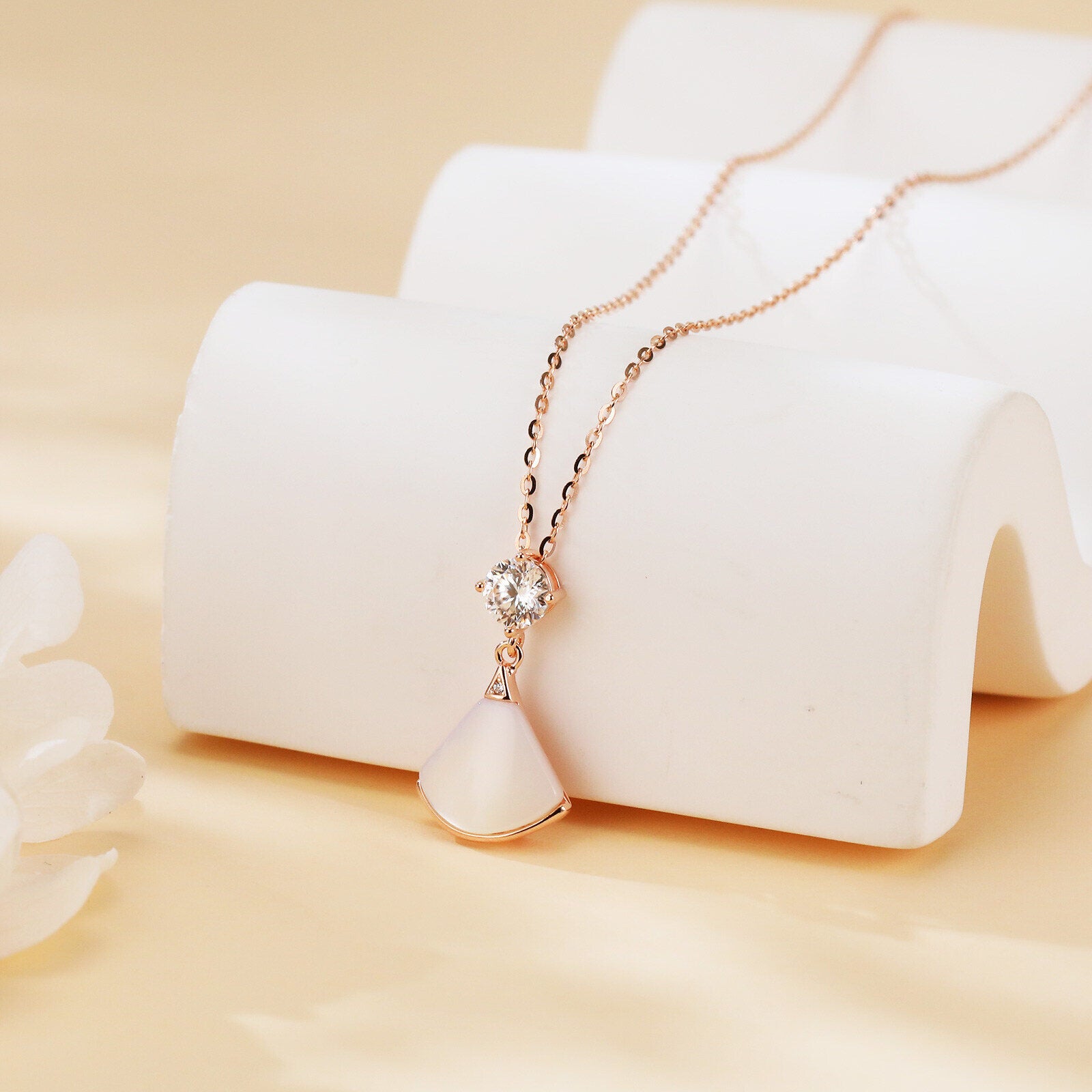 Rose gold necklace with a diamond pendant on a white stand against a beige background