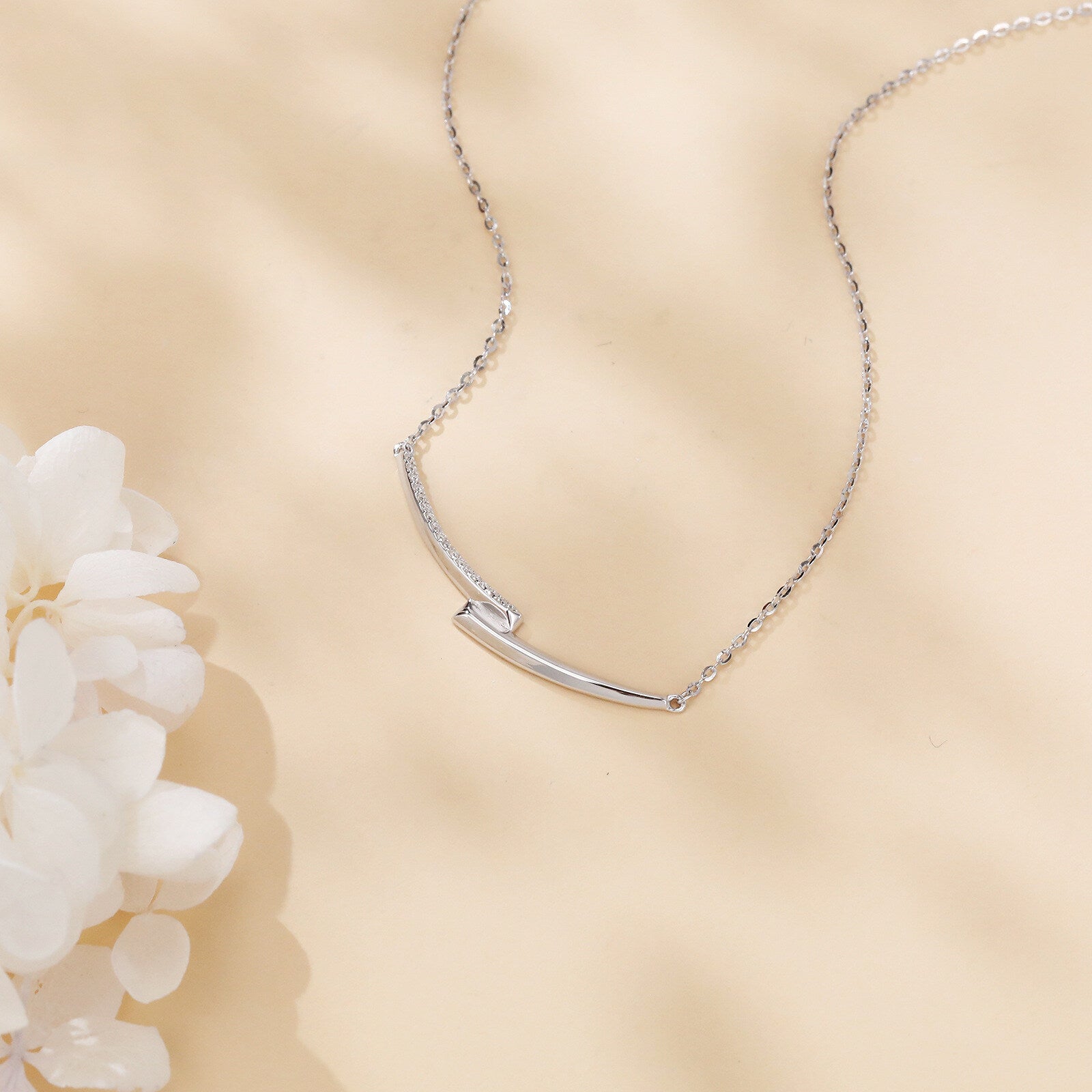 Silver necklace on a beige background with a white flower