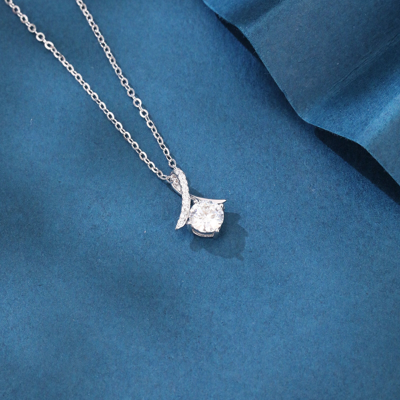 Silver necklace with a diamond pendant on a blue fabric background