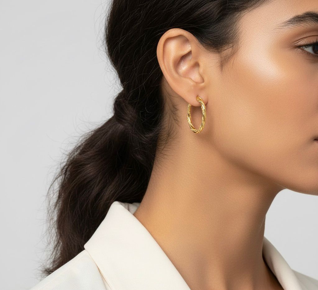 Close-up of a person wearing gold hoop earrings with a neutral background