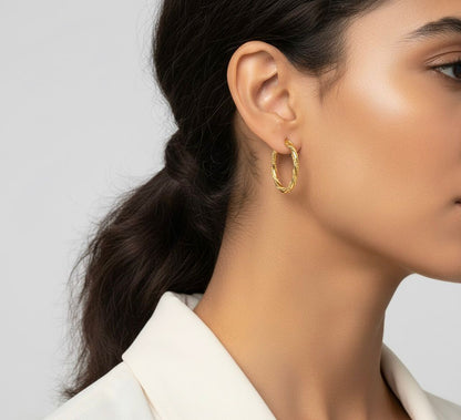 Close-up of a person wearing gold hoop earrings with a neutral background